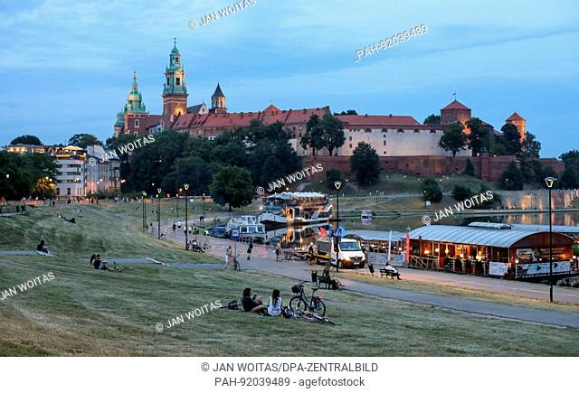 Many people sit on a meadow on the bank of the Vistula river in Krakow (Poland). In the background is Wawel Castle. Taken 22.06.2017