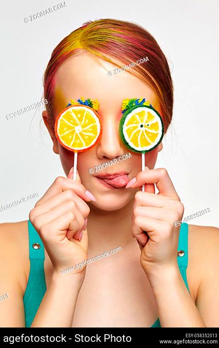 Teenager girl with unusual face art make-up show tongue. Child with lollipops in hands closing eyes. Sweet tooth concept