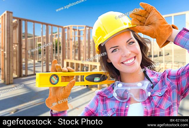 Female construction worker holding level wearing gloves, hard hat and protective goggles at construction site