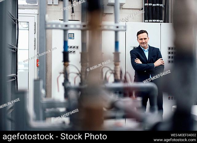 Smiling businessman standing with arms crossed in front of machinery