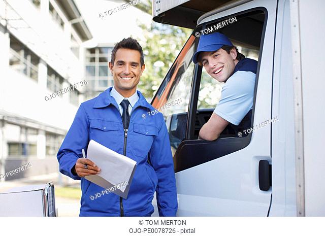 Worker with clipboard standing with truck and driver