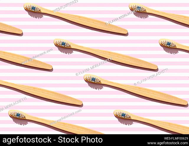 Pattern of wooden toothbrushes flat laid against pink striped background