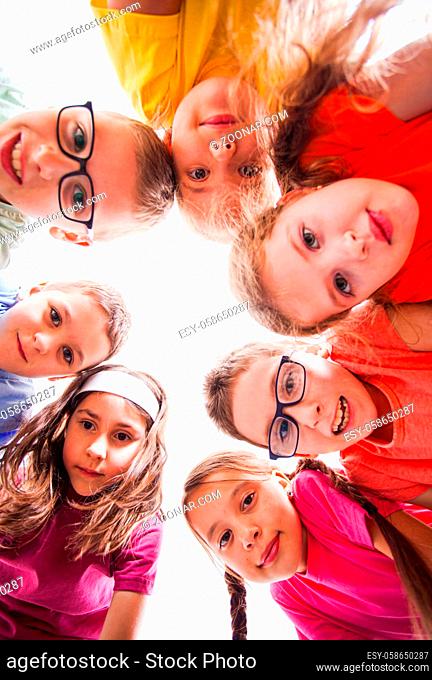 Cute boys and pretty girls looking at camera, view from down. Team of kids outdoors. Summer camp and holidays