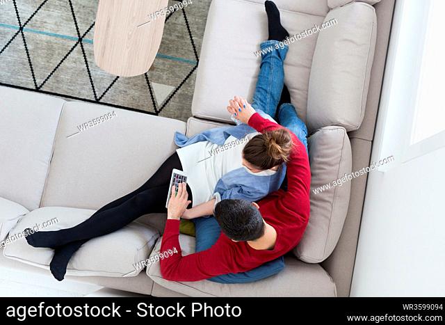 Young couple relaxing at home using tablet computers reading in the living room on the sofa couch