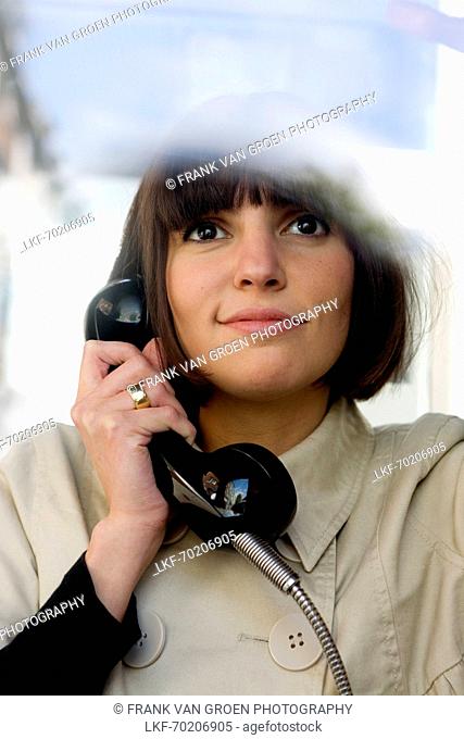 Young woman calling from a public telephone booth, Duesseldorf, North Rhine-Westphalia, Germany