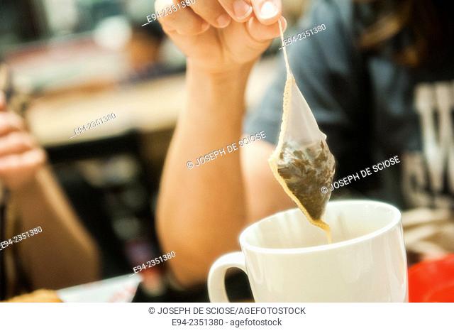 Partial view of a woman holding a tea bag over a white cup