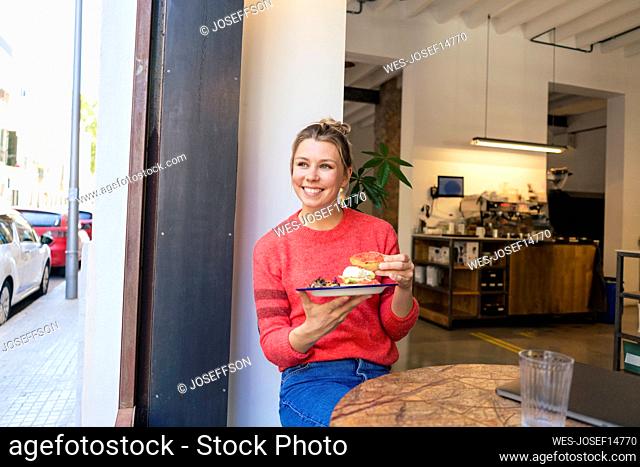 Happy freelancer sitting with plate of food at table in cafe