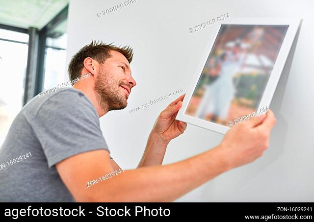 Mann als Heimwerker beim Aufhängen von Bild oder Bilderrahmen im neuen Zuhause