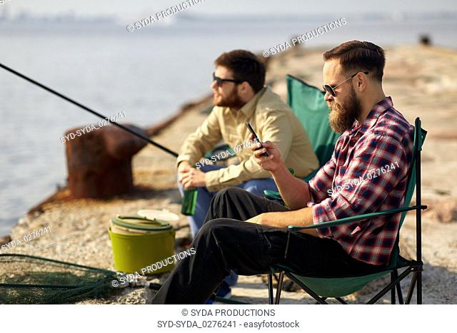 friends with smartphone and beer fishing on pier
