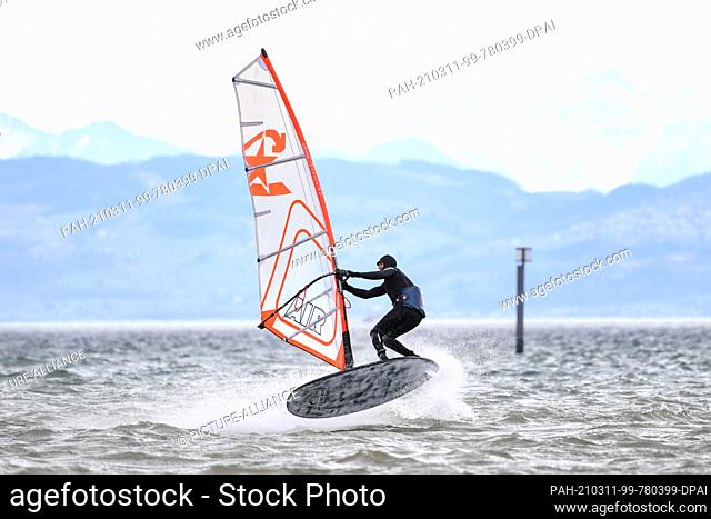 11 March 2021, Baden-Wuerttemberg, Friedrichshafen: A surfer jumps with his surfboard over Lake Constance in front of Fischbach