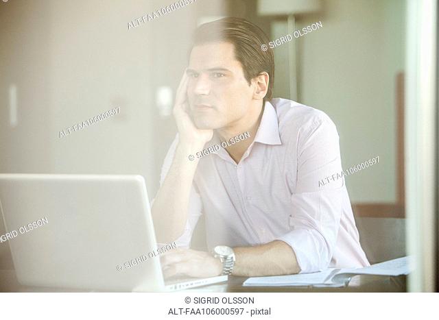 Man sitting before laptop computer, daydreaming in office