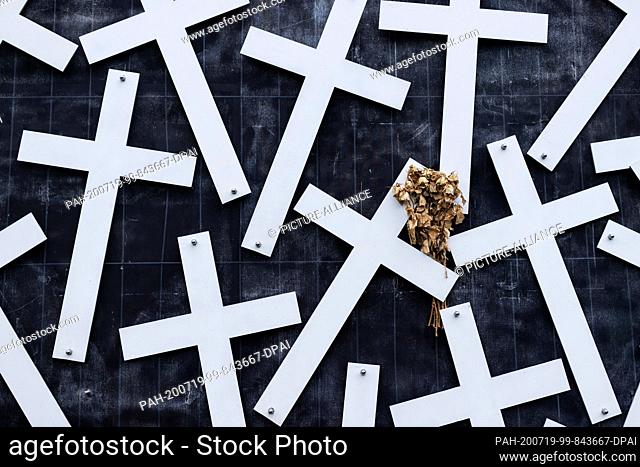 16 July 2020, North Rhine-Westphalia, Duisburg: Withered roses are stuck on a cross at the memorial for the victims of the Love Parade catastrophe