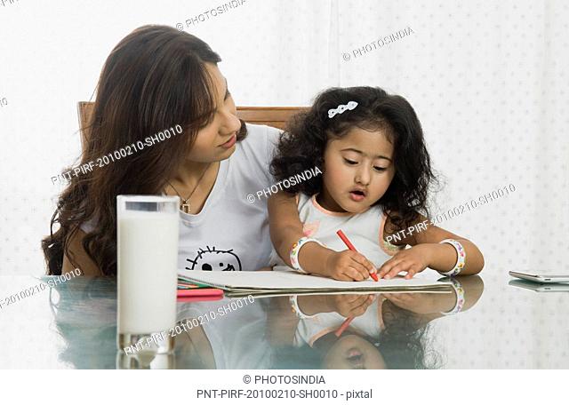 Close-up of a girl drawing with her mother at the dining table
