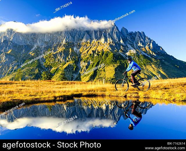 Mountain biker in front of mountain scenery reflected in a mountain lake, Mandlwand, Hochkönig, Berchtesgaden Alps, Mühlbach am Hochkönig, Pongau, Salzburg