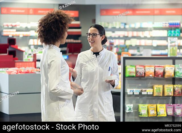 Two friendly female colleagues talking about medicines and prescriptions while working together as pharmacists in a modern drugstore