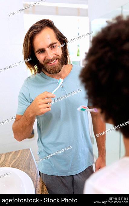 Diverse couple standing in bathroom brushing teeth