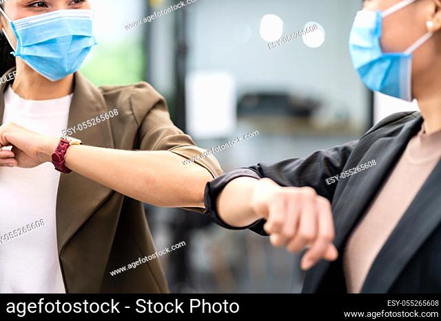 Close up two businesswomen do alternative greeting in new normal office lifestyle. They wear protective face mask and use elbow touch instead of hand shake to...