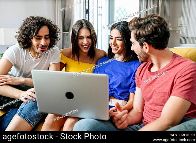 Smiling multi-ethnic friends sharing laptop while sitting in living room