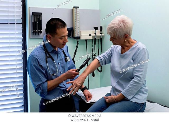 Young Asian male doctor examining a senior patient with magnifying glass in the clinic