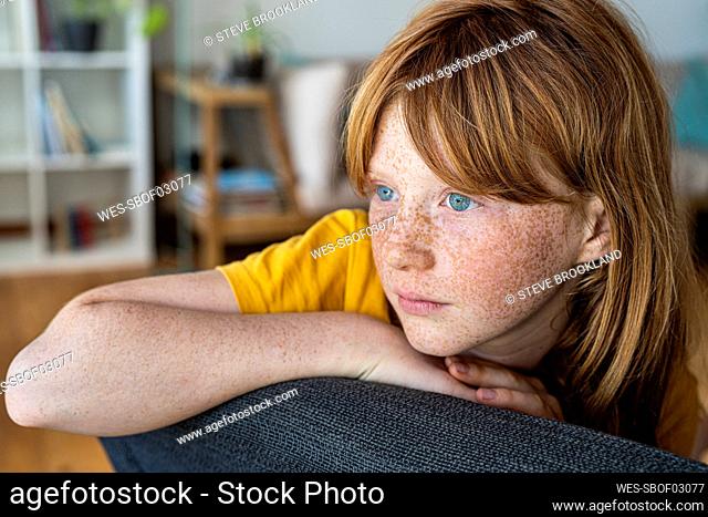 Contemplating redhead girl sitting on chair at home