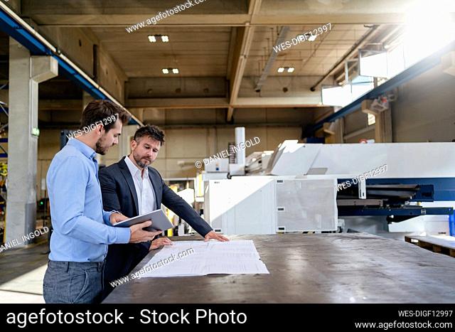 Businessmen with digital tablet and blue print standing at factory
