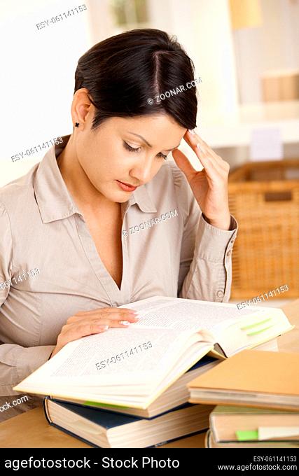 College student learning at desk at home, reading book, concentrating