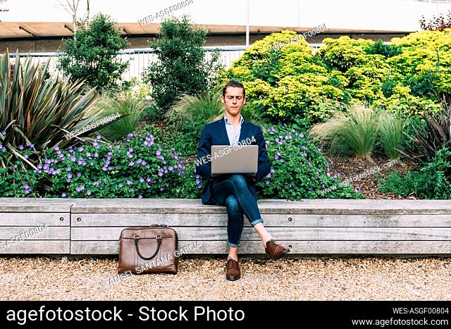 Businessman using laptop while sitting on bench at park