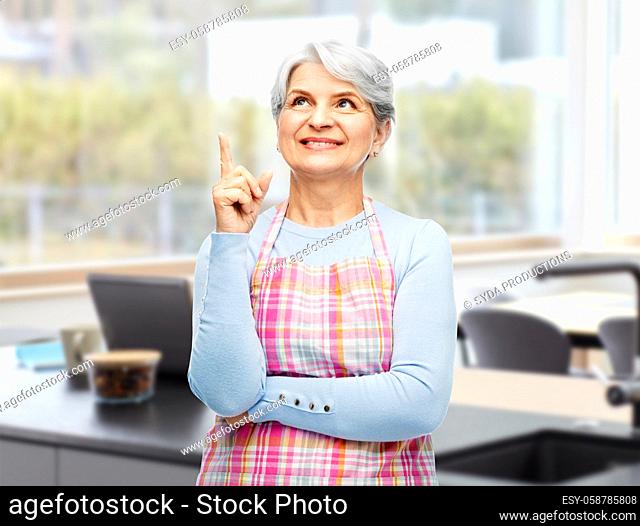 smiling senior woman in apron pointing finger up
