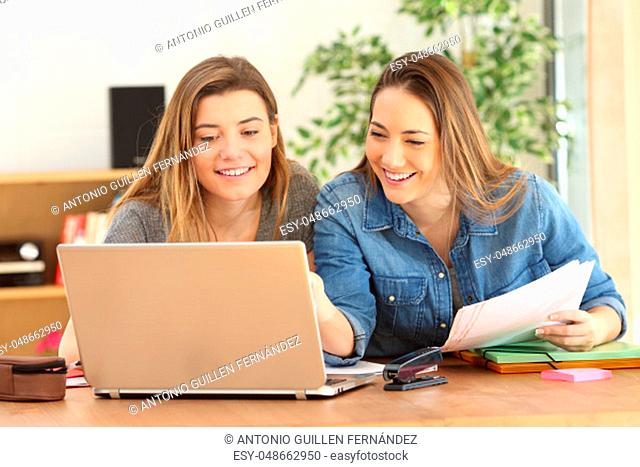 Two students studying together on line with a laptop in the living room at home with a homey background