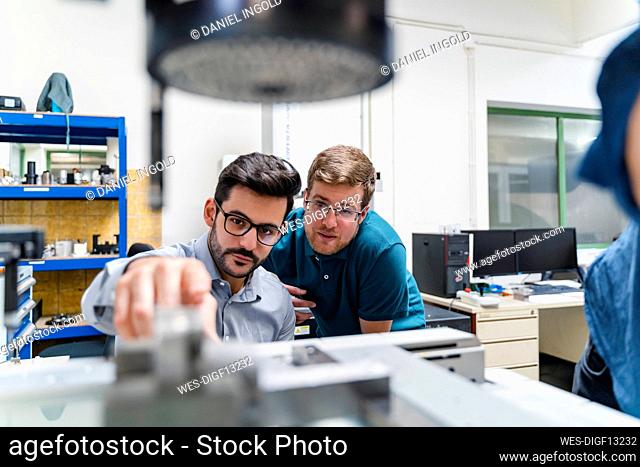 Businessman and male colleague examining surveyor machine in manufacturing factory