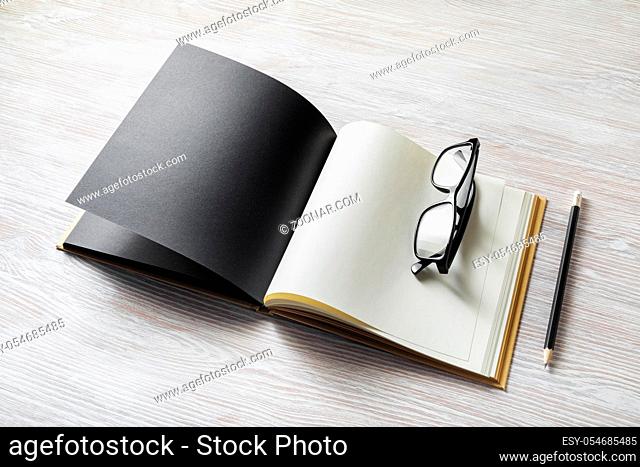 Photo of open book with blank pages, glasses and pencil on light wooden background. Responsive design template