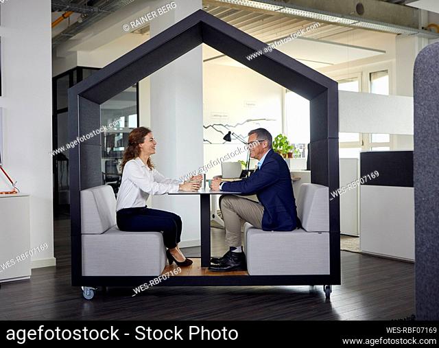 Smiling businessman and businesswoman sitting in a wheeled cubicle in office