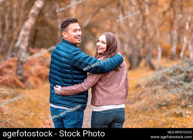 Smiling couple looking over shoulder while standing in park during autumn