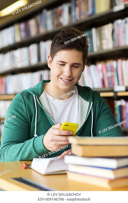 people, education, technology and school concept - male student with smartphone and books texting message or networking in library