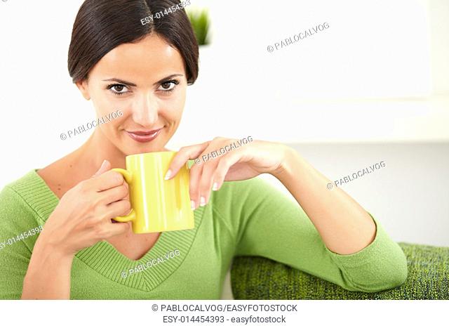 Attractive lady in green shirt holding a coffee cup while looking at the camera