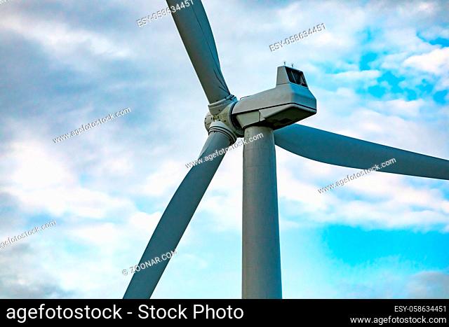 A low angle and close up shot on the nacelle, cover housing of generating components, of a wind turbine with three blades against a broken cloud sky