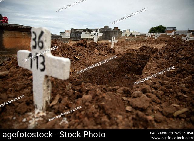 06 March 2021, Brazil, Rio De Janeiro: A simple cross with no name and a number stands at an open grave at Iraja Cemetery