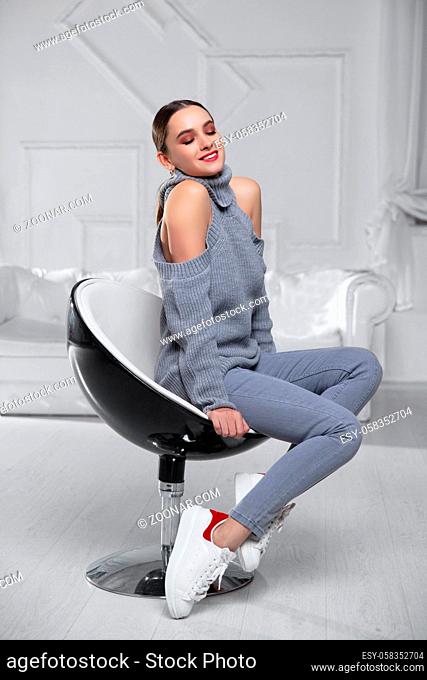Happy brunette wearing a gray sweater and jeans posing in studio