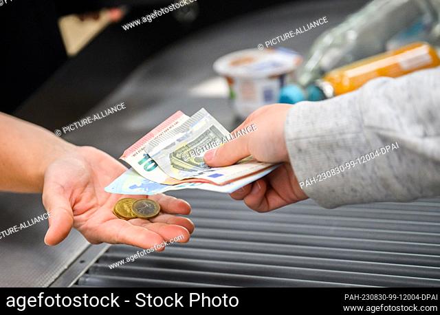 30 August 2023, Lower Saxony, Hanover: A cashier gives a customer change at the checkout of a supermarket. The Federal Statistical Office announces the...