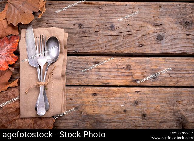 Multiple autumn leaves and cutlery set over a napkin on wooden surface