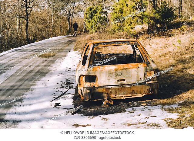 Burnt out car by side of icy road with man walking in distance, Sweden, Scandinavia