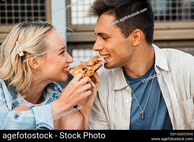happy couple eating pizza outdoors