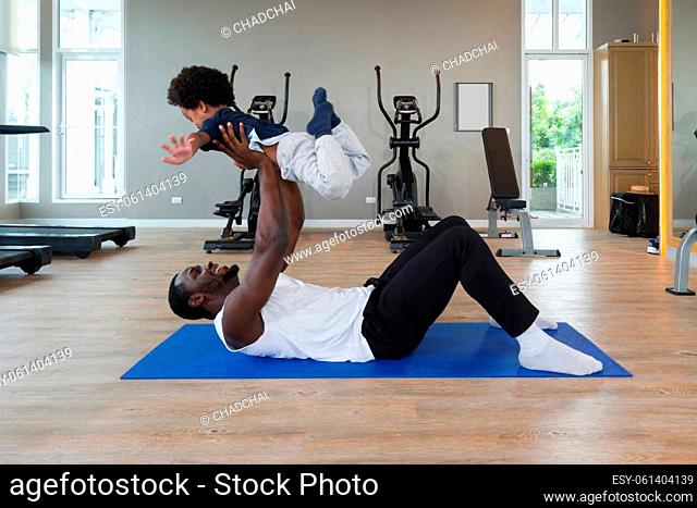 Young short curly black hair father with moustache and beard in sportswear playing with his son after finish exercise routine on yoga mat
