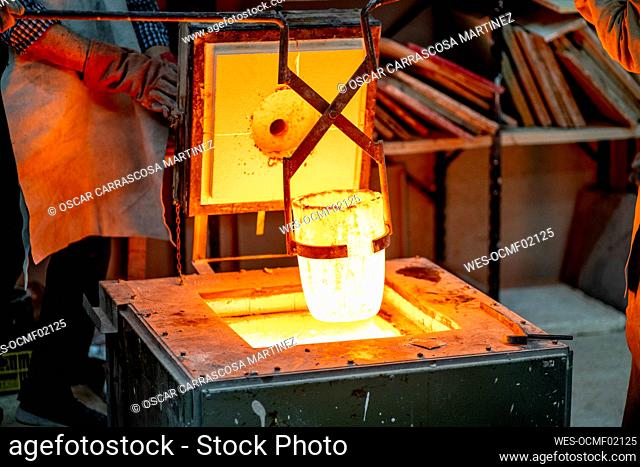Manual worker removing melted bronze container from furnace at workshop