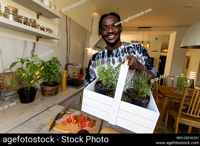 Smiling man holding basket with rosemary and thyme plants at home