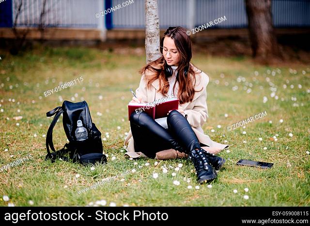 female student virtual learning on mobile internet outdoors. Girl online learning courses using smartphone sitting in park