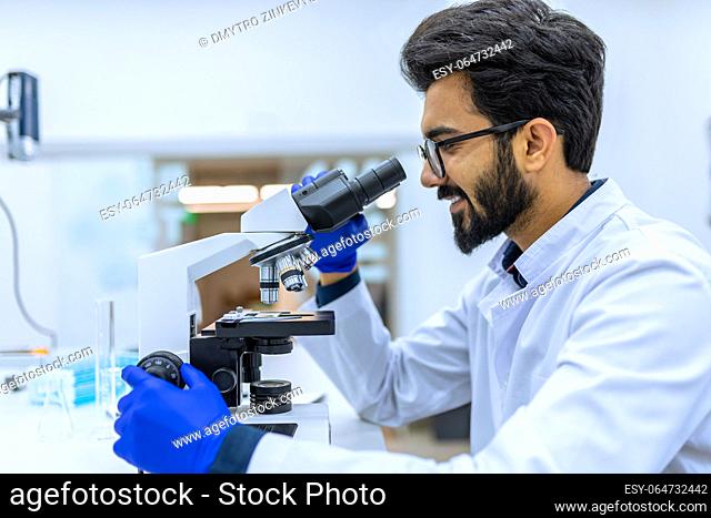 Dark haired scientist conducts experiments, adjusts specimen in petri dish and looking on it into microscope, researching in modern laboratory