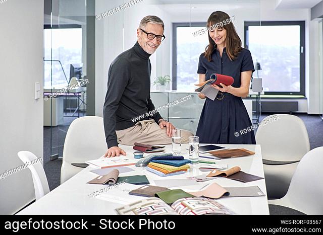 Smiling creative businessman and businesswoman with swatches in office