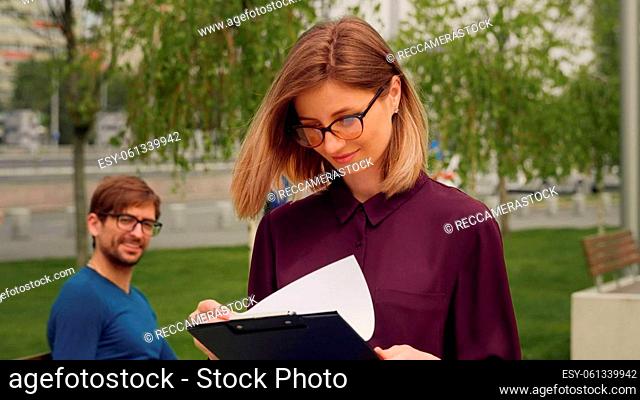 Confident Businesswoman walking out of Business building. Young blonde Woman greets friend sitting on a bench while the Walk. Success
