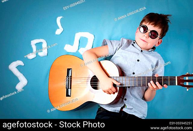 happy seven years old boy on blue blanket background with acoustic guitar and musical notes. Young guitarist singing song